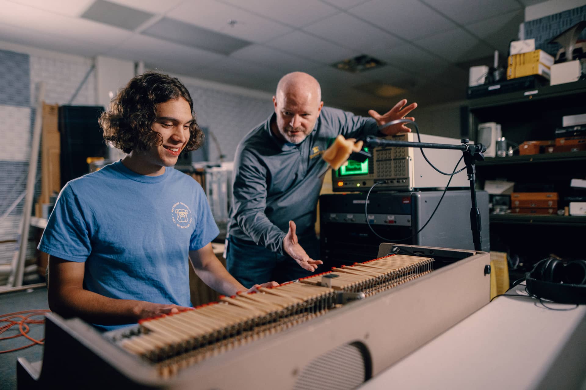 A Kettering student plays an electronic keyboard in the Acoustic Lab. A professor listens and gestures with his hands.