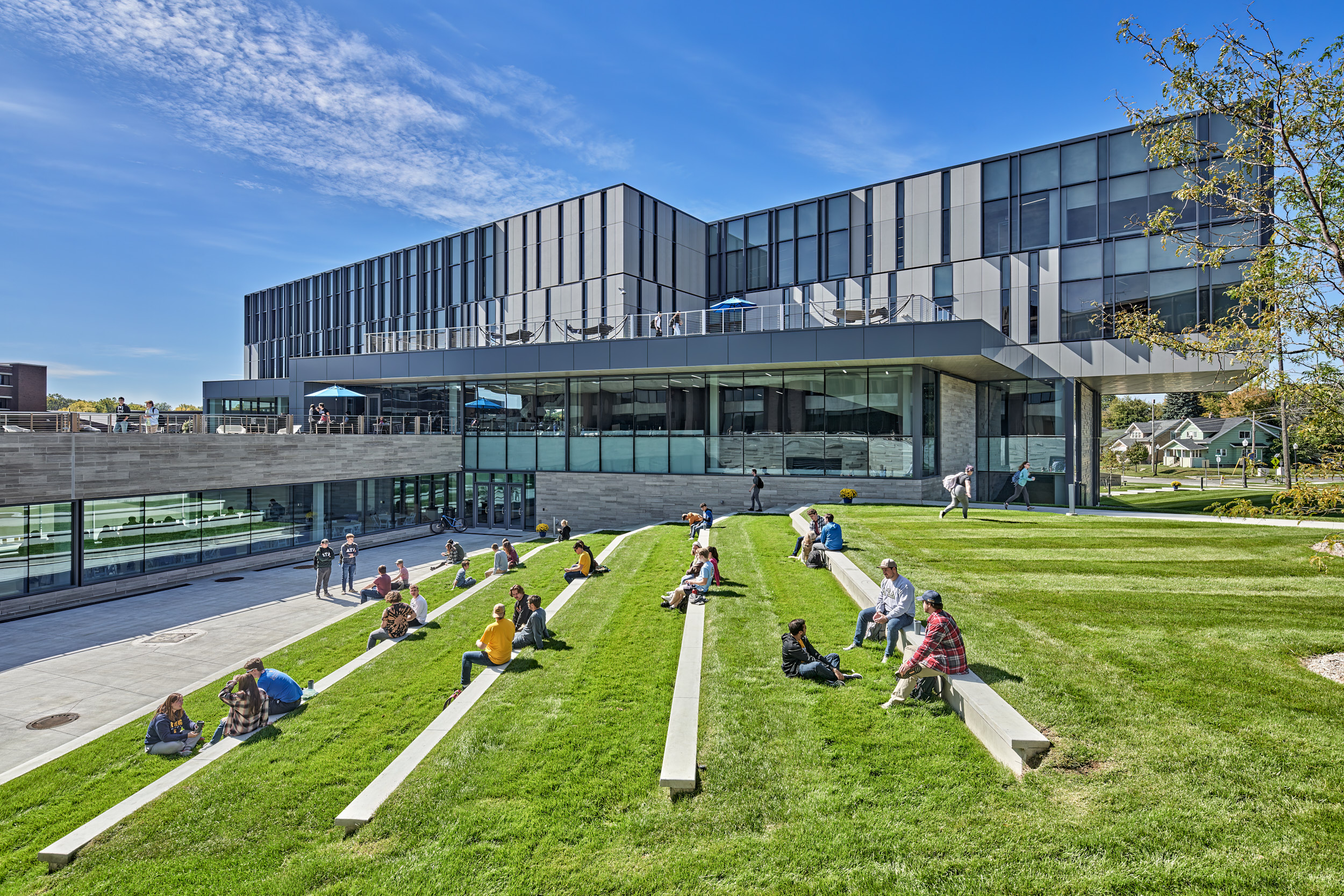 Students at Kettering University lounge on a lawn outside the Learning Commons on a sunny day.