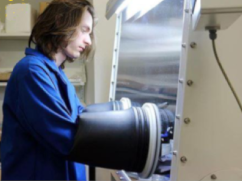 A student works meticulously in a controlled environment at Kettering University's Advanced Energy Storage and Applications Laboratory, utilizing a glove box to ensure precision and safety.