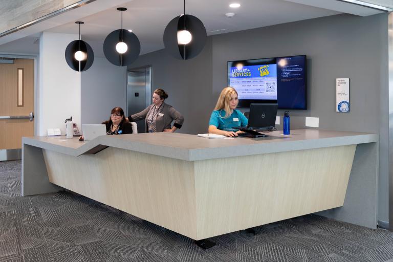 The welcoming library services desk at the Learning Commons provides support and resources to enhance the student experience.