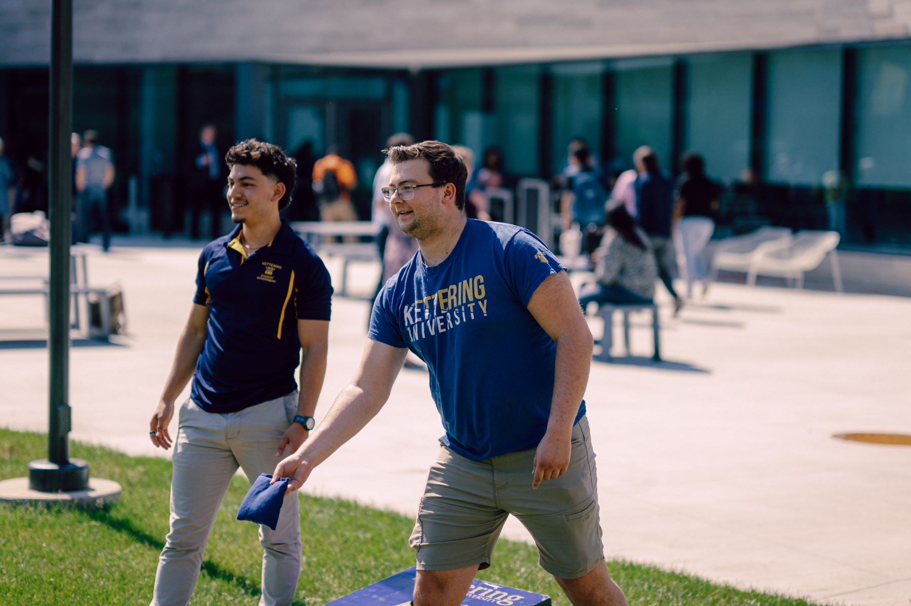 Two Kettering students play cornhole by the Learning Commons. One student holds a bean bag and readies his throw.