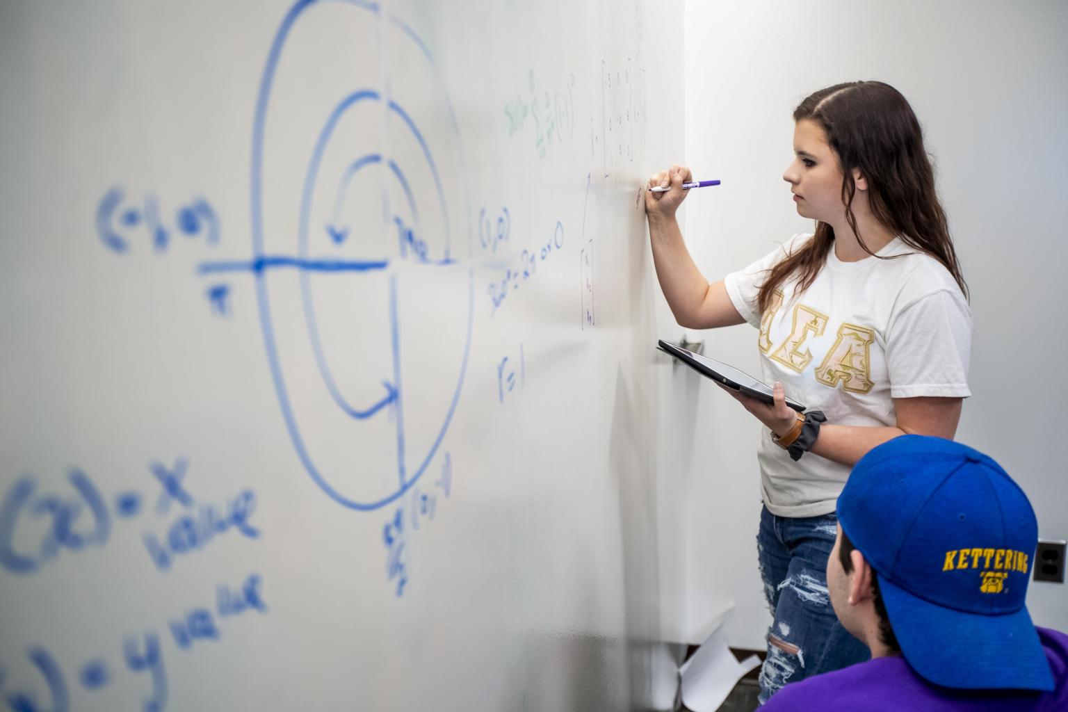 A student works on a homework problem at a white board in a dspace.