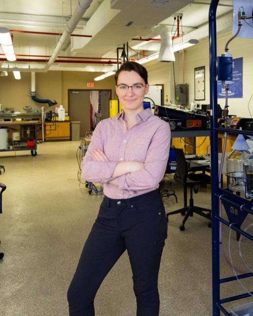 Kettering chemical engineering alum Ashley Switalski stands in a lab next to chemical engineering equipment