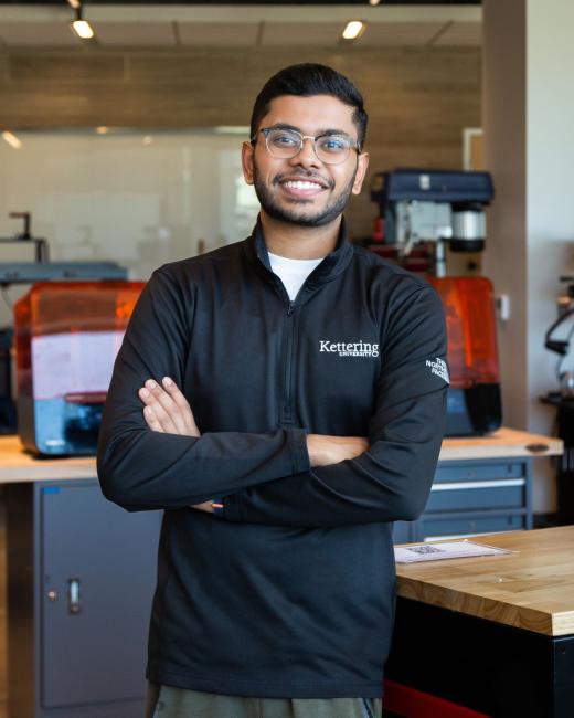 Kettering computer science alum Hemanth Tadapelli wears a Kettering jacket and stands in Kettering's Makerspace