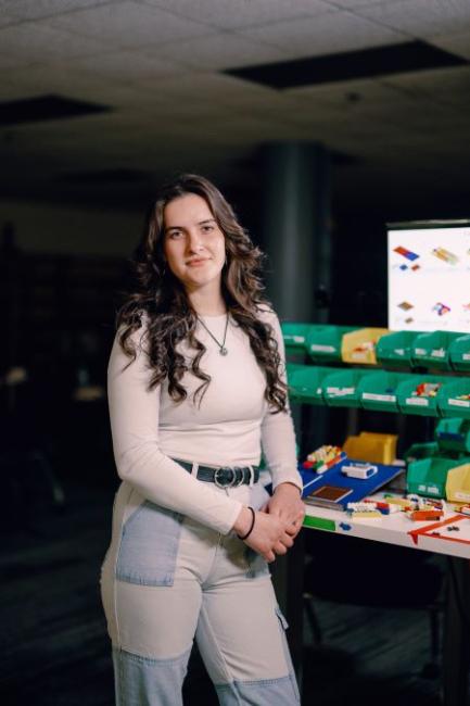 Kettering student Samantha Kneebone stands in the Lego Lab. A monitor shows Lego designs and containers hold colorful bricks.