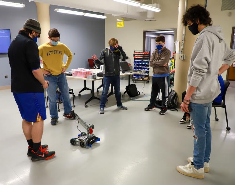 Kettering University students stand in a circle around a robot.