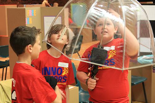 Three elementary students working an on umbrella device.