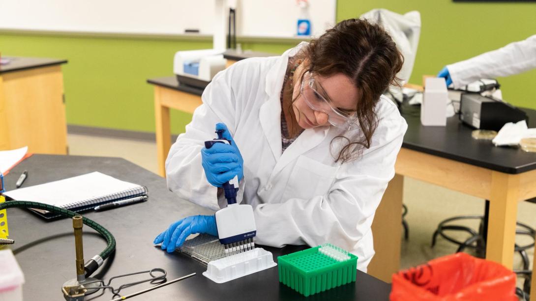 A student in a lab coat and goggles conducts an experiment in a science lab