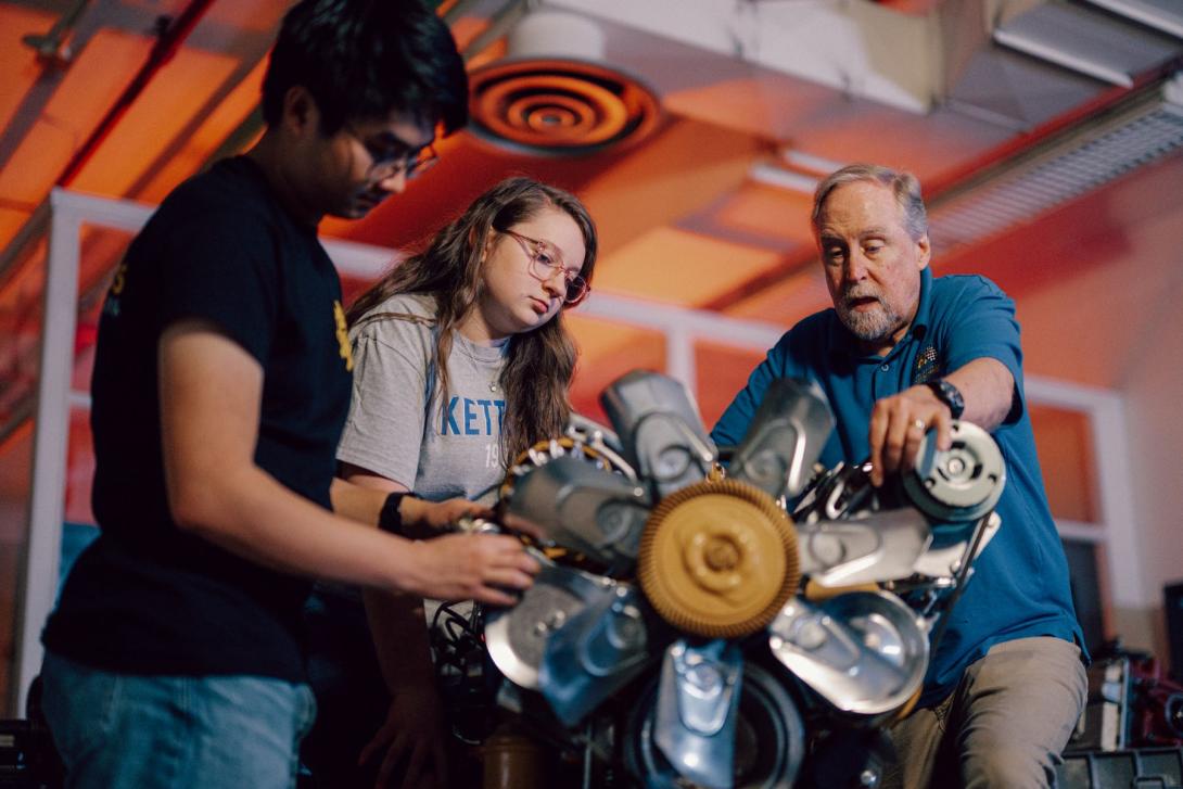 Two Kettering mechanical engineering students and a professor look closely at a car part in the Car Lab