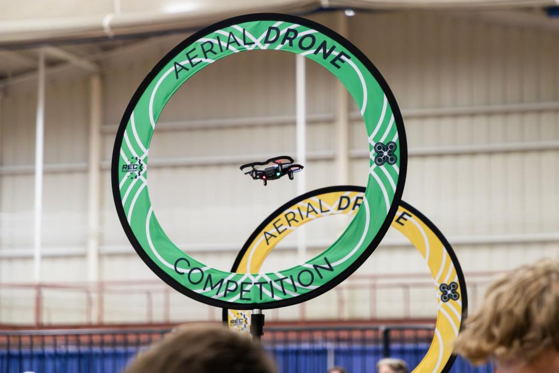 A drone flies through a green ring, with a yellow ring beyond it.