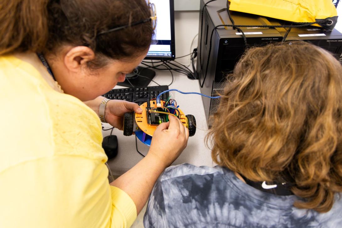 An instructor and young student in Kettering's Pre-College program study the wiring of a small yellow robot