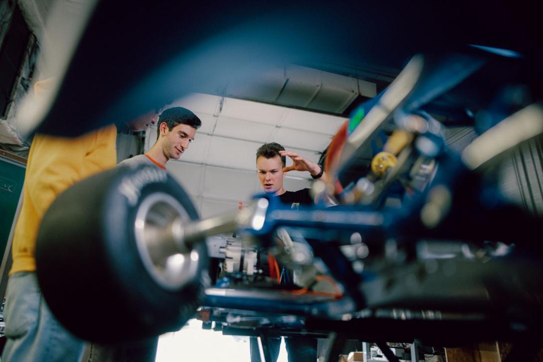 A group of Kettering electrical aengineering students stand over an electric vehicle and gesture toward it