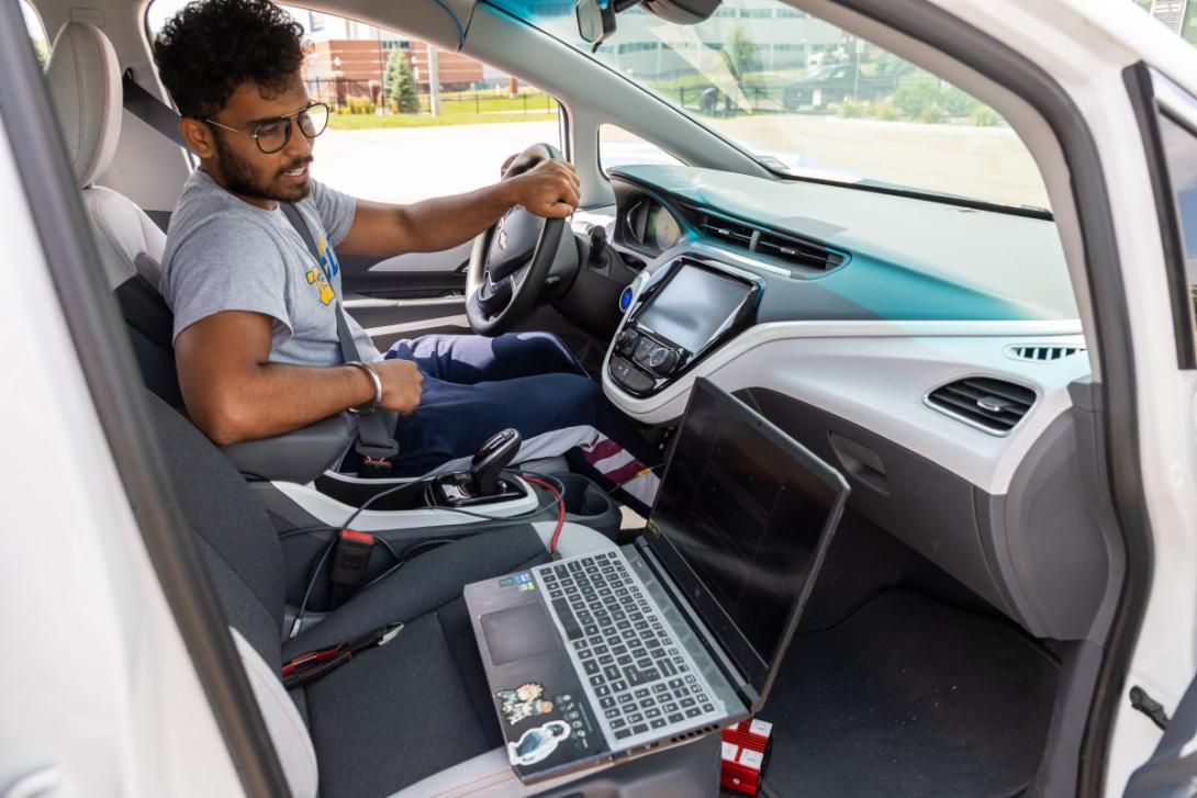 A Kettering graduate student sitting in a car reads the output from the car's computer via a laptop on the passenger seat.