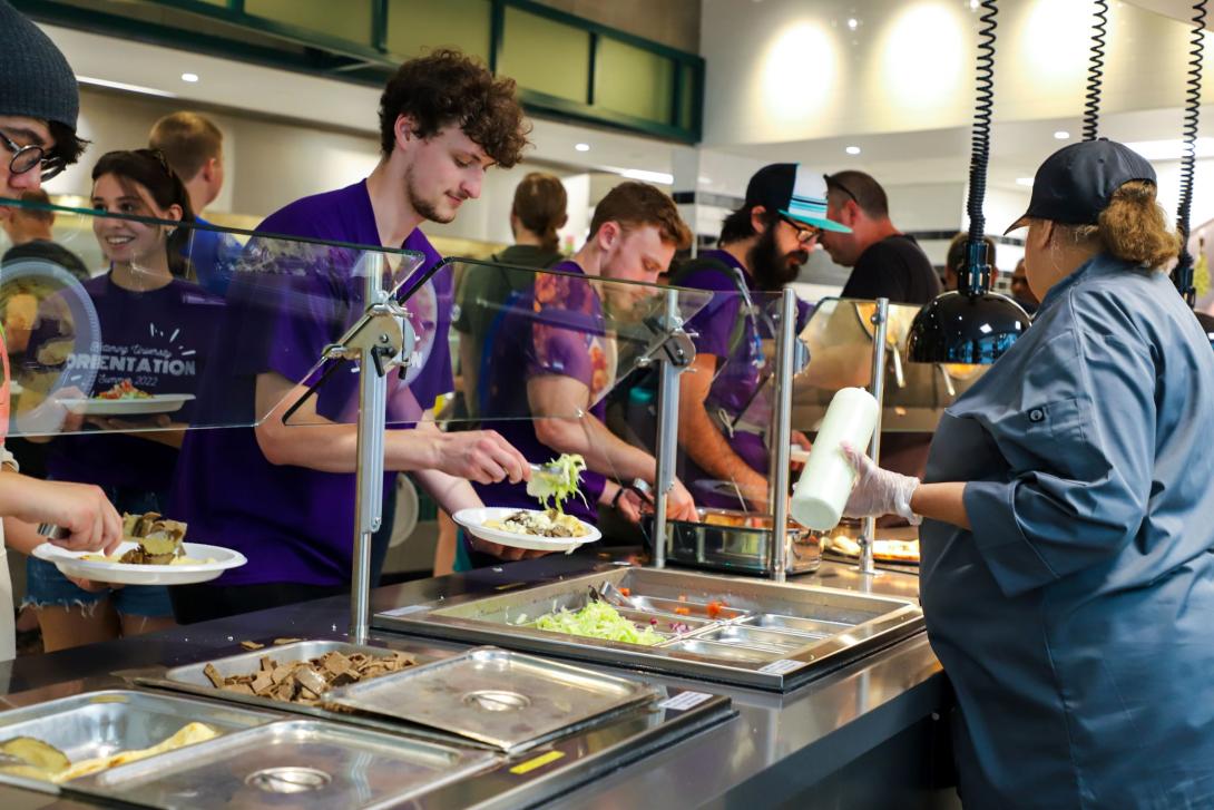 Kettering students add food to their plates from a buffet line in Battenberg Cafe. A cafeteria worker helps serve them.