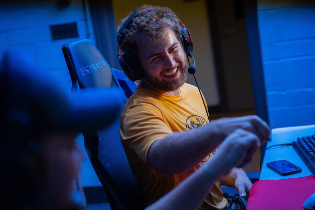 Two Kettering E-sports players smile and fist bump one another. One student wears a gaming headset.