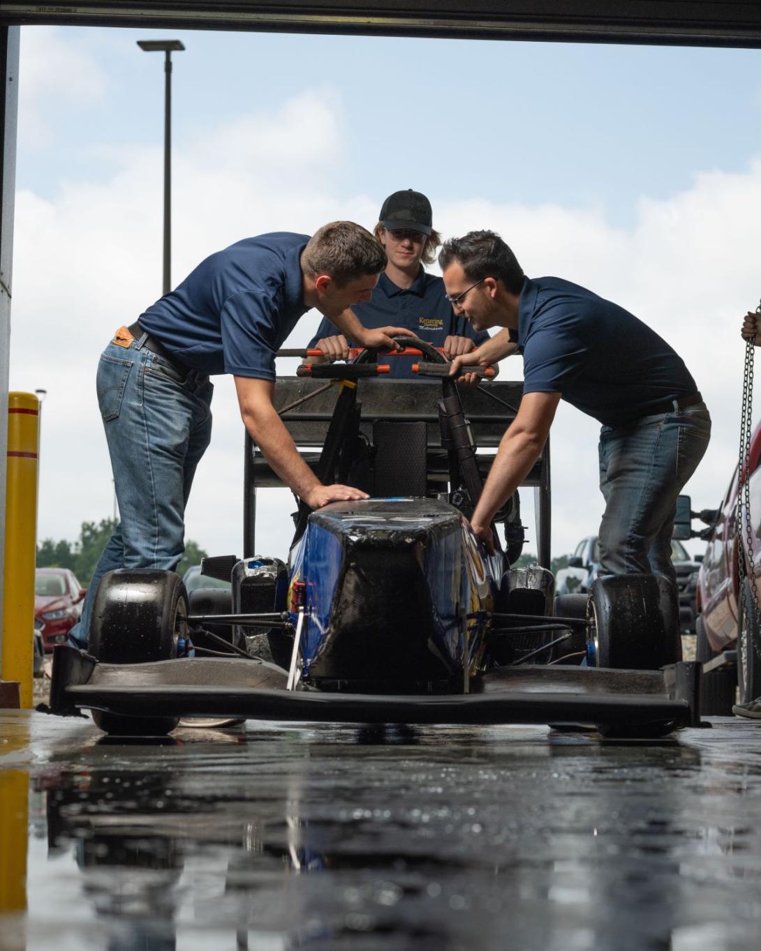 Three Kettering students examine a formula-style racing car inside the SAE Garage