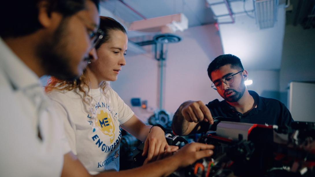 Three Kettering mechanical engineering students inspect car parts in the Car Lab