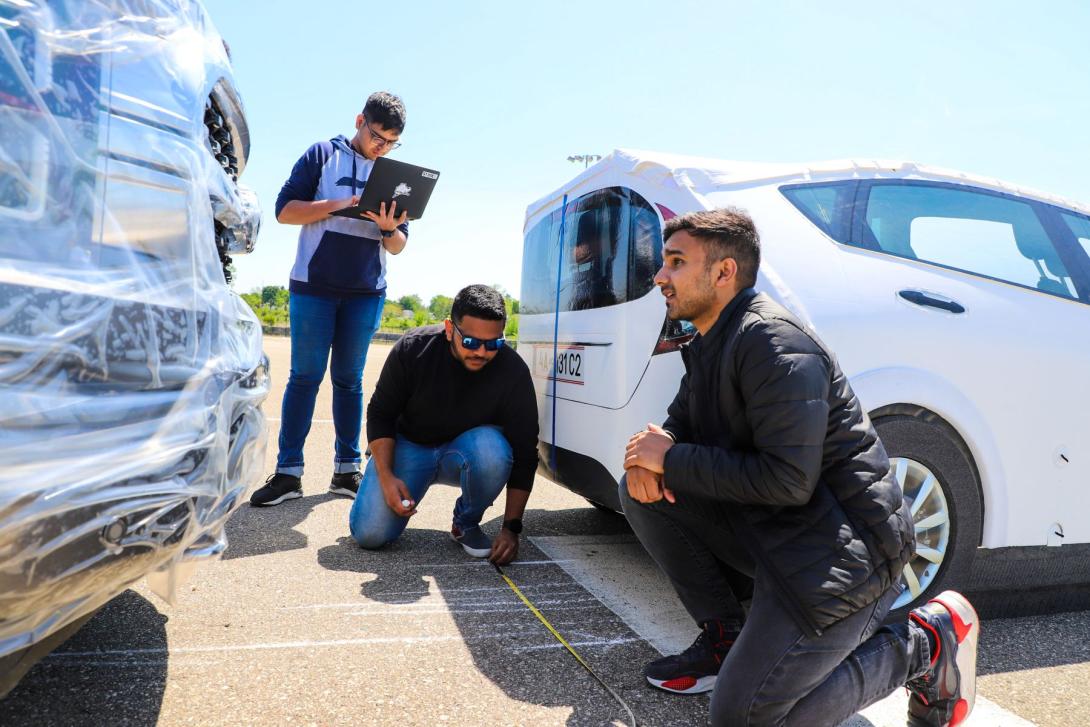 Three Kettering students at the Mobility Research Center measure markings on a road using measuring tape. One holds a laptop