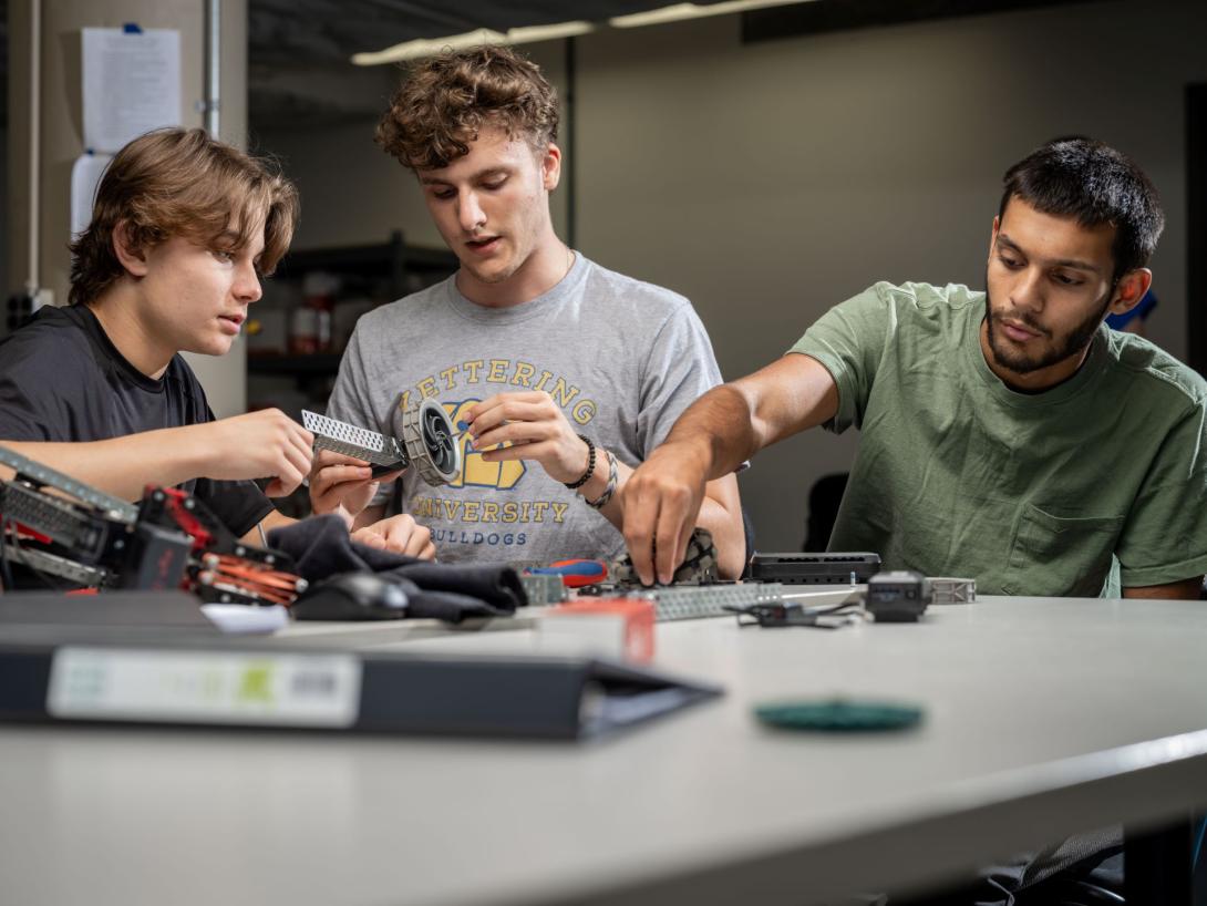 Three Kettering industrial engineering students inspect different machine parts and fit them together