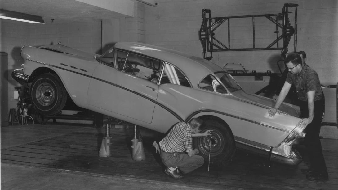 A black-and-white photo from the 1950s-1970s of two Kettering students inspecting a car tire in an automotive bay