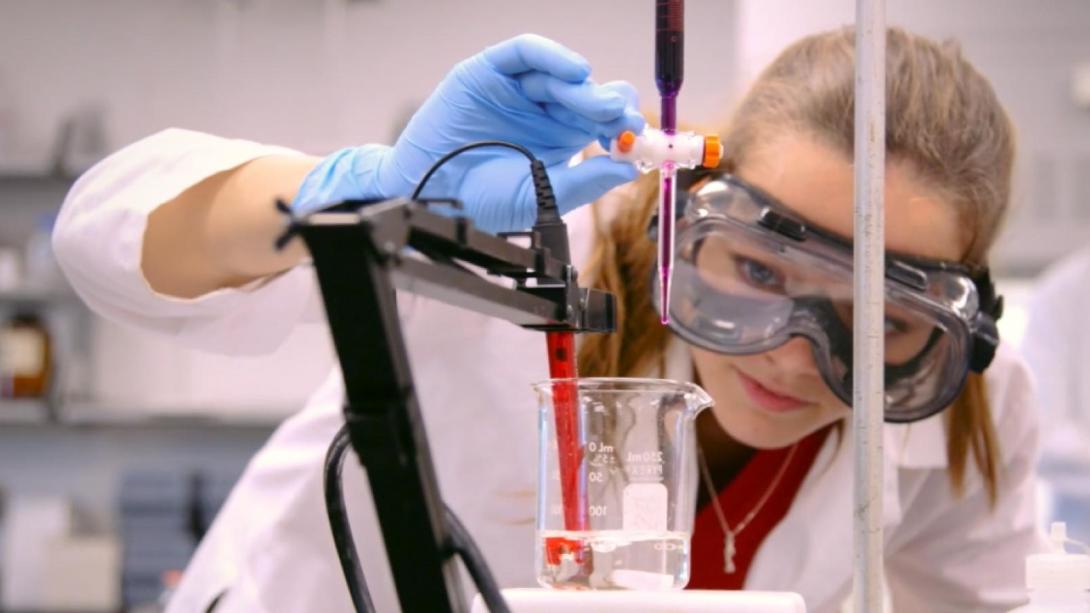 A student in a lab coat and goggles conducts a science experiment