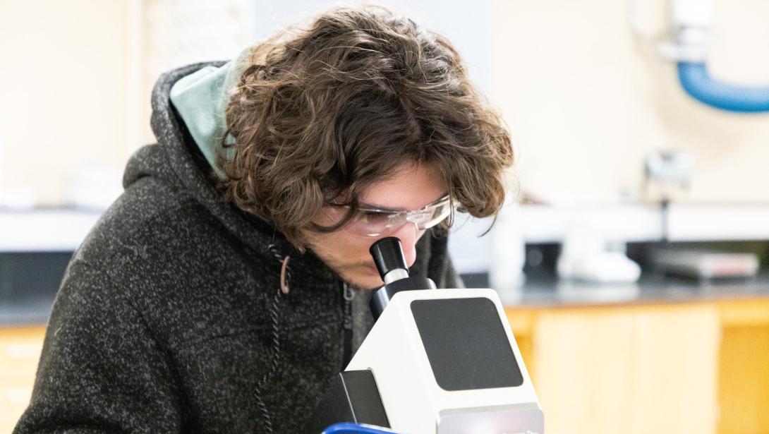 A student looks into a microscope in a science lab setting