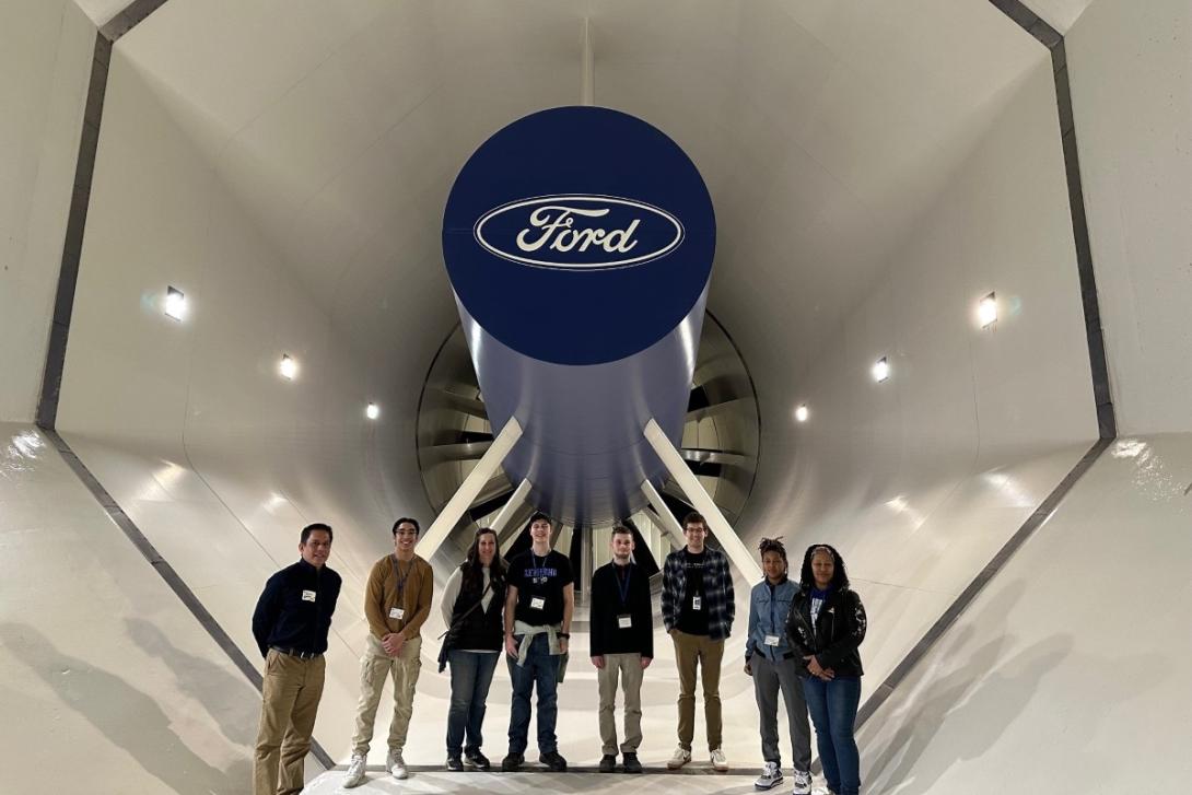 A group of eight individuals stand underneath a Ford logo