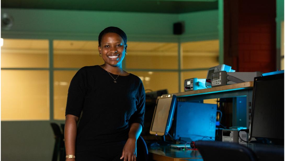 An individual in business attire poses in front of a desk with equipment