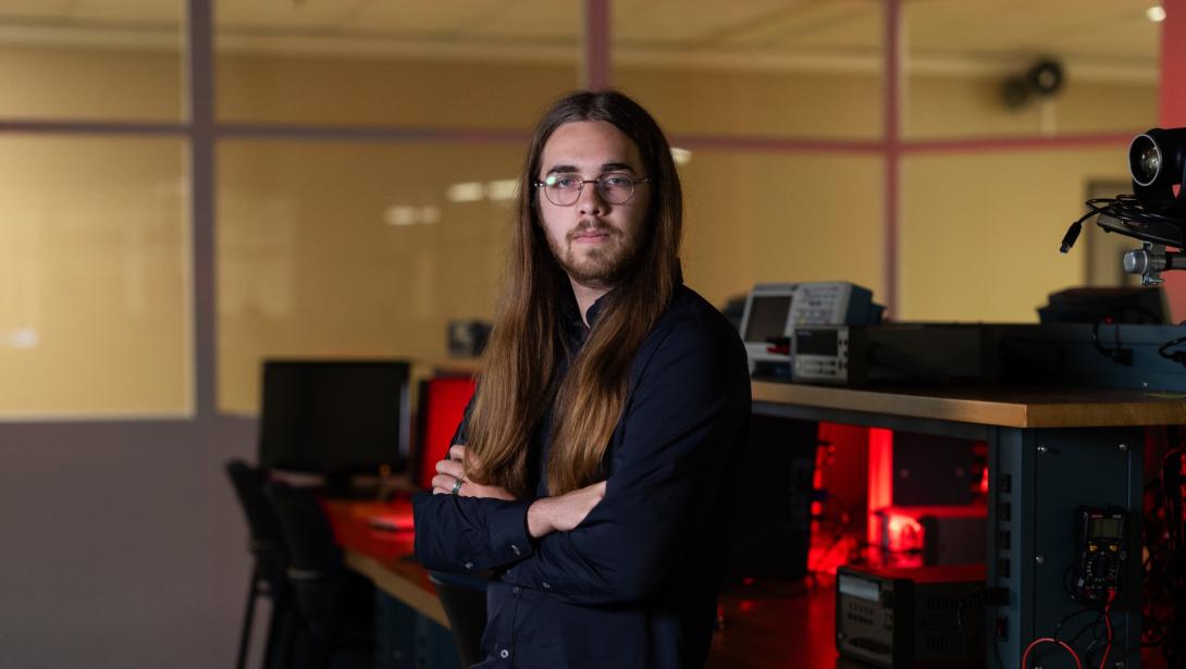 An individual in business attire stands with arms crossed in a classroom