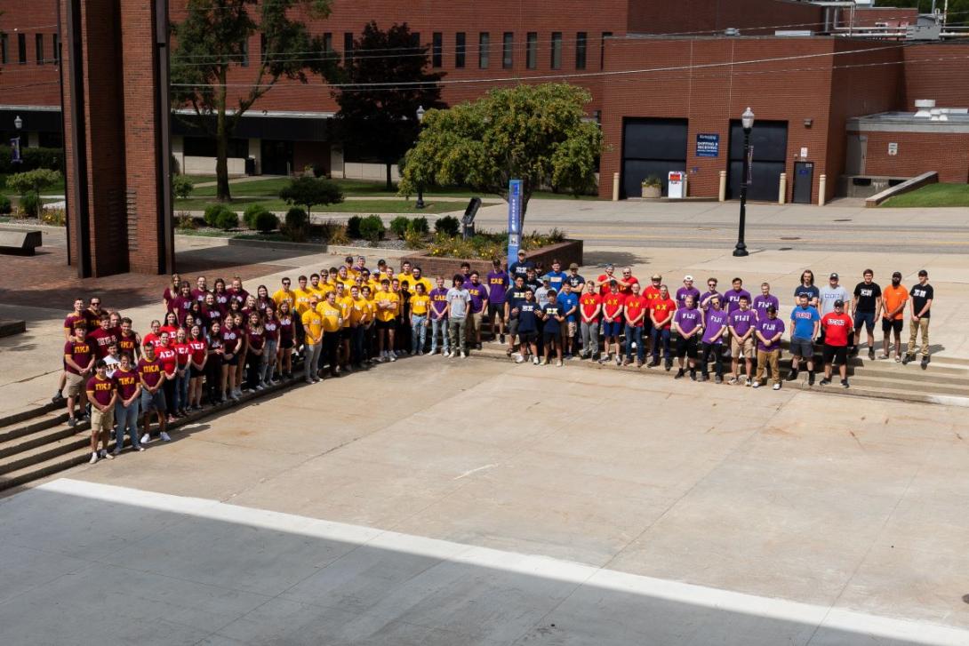 Kettering Greek Life students wearing shirts that represent each fraternity or sorority pose for a group photo outside