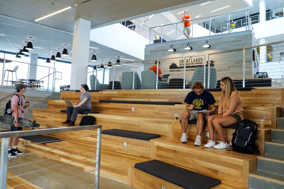 Multiple groups of students study and chat while seated on wooden benches inside Kettering's Learning Commons