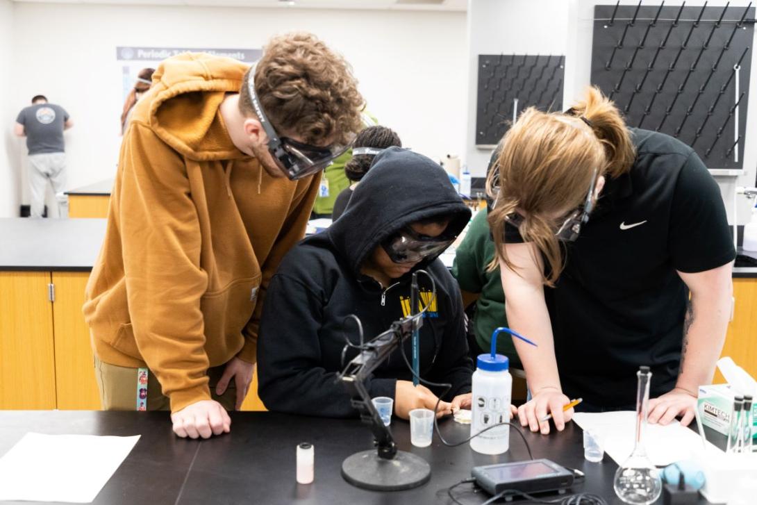 Three people crowd around a microscope