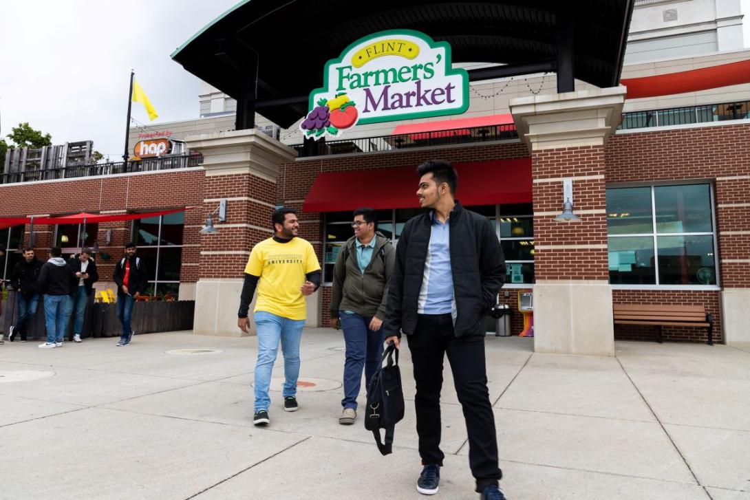 Three students walk outside the entrance of the Flint Farmers' Market