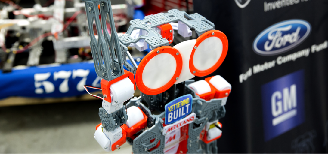 A close-up of a "Kettering Built" robot at Kettering University's robotics center, with sponsor logos in the background.