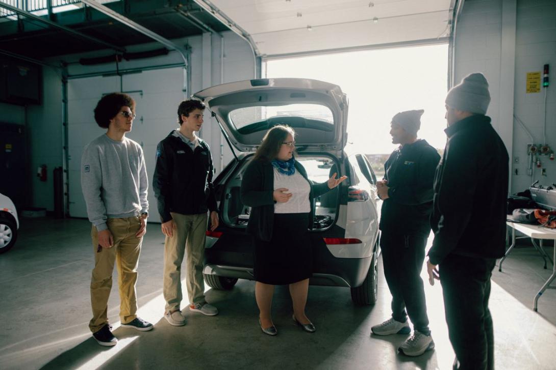 A group of people stand around the back of a car with the trunk hatch open