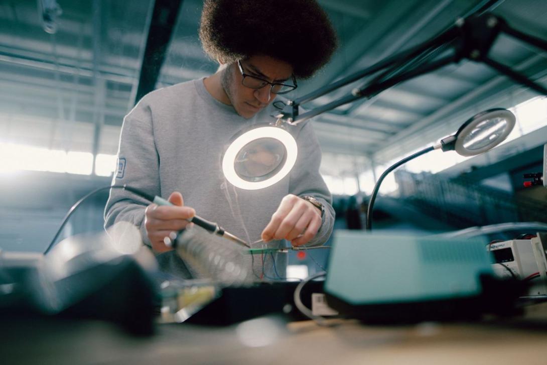 A Kettering electrical engineering student looks through a magnifying glass to couple electrical wires