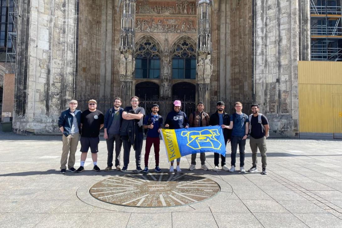 Kettering students stand in front of a historic church in Germany and hold up a Kettering banner