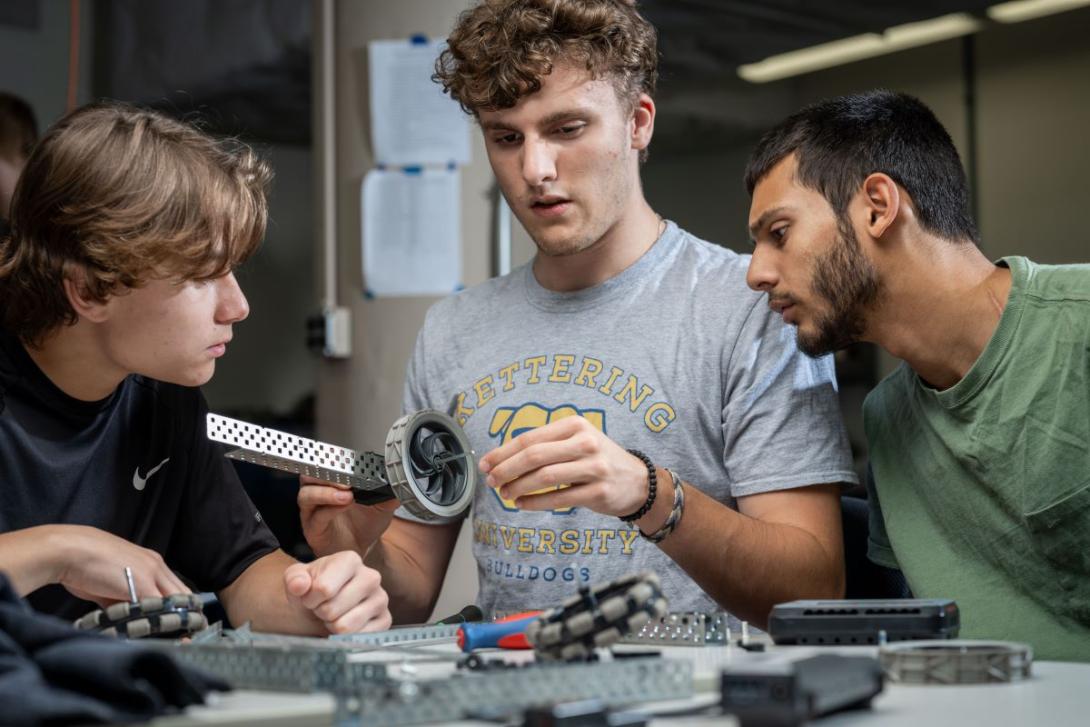 Three Kettering industrial engineering students work on machine parts