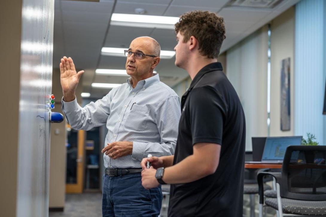 A School of Management Kettering professor teaches a student as both stand in front of a whiteboard